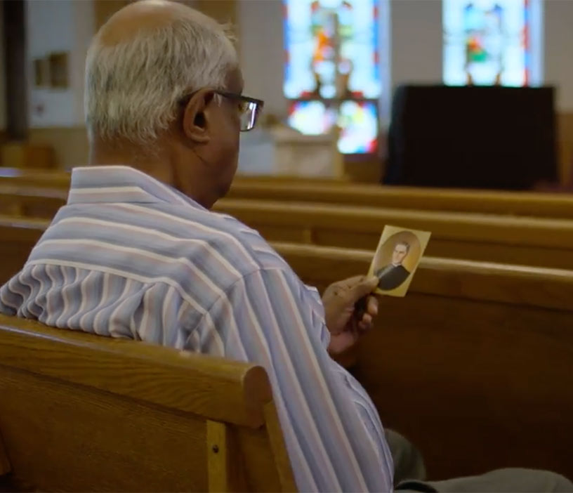 Man looking at a picture of Father McGivney while sitting in a church pew.