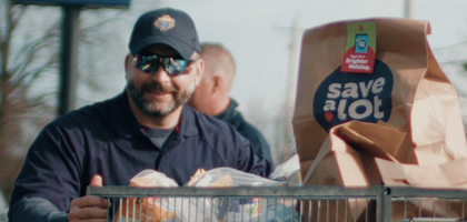 A man with a Knights of Columbus hat pushing a large bin full of groceries. 