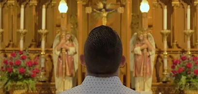 A man stands in front of an altar looking at the Crucifix.