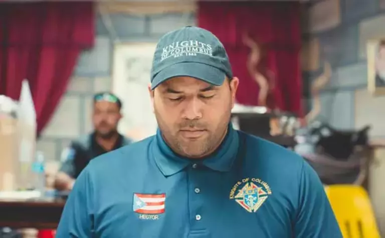 A man with a Knights of Columbus shirt has his eyes closed and appears to be praying.