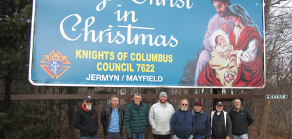 Members of Sacred Heart of Mary Council 7622 in Jermyn, Pa., standing outdoors dressed in winter coats and winter hats assemble in front of the council’s annual reminder to the community to Keep Christ in Christmas.