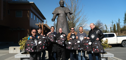 Members of Holy Name Council 8712 in Vancouver, British Columbia, stand with chaplain Msgr. Gregory Smith (center) in front of the Archdiocese of Vancouver’s John Paul II Pastoral Centre, displaying backpacks filled with supplies for babies undergoing substance withdrawal therapy. 