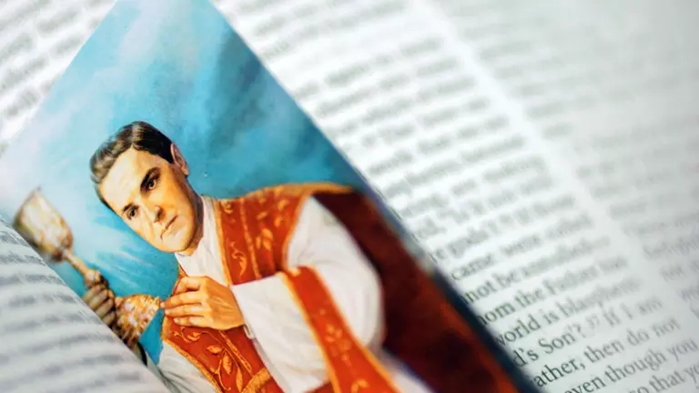 A Fr Michael McGivney prayer card illustration with him holding a chalice resting in an open page of a bible.
