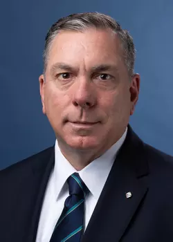 Portrait photo of Maj. Michael McCusker in a black suit with white dress shirt and a blue and teal tie.