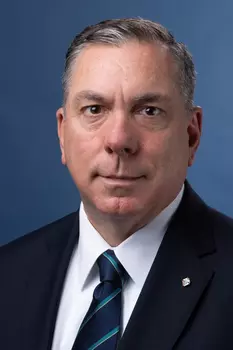 Portrait photo of Maj. Michael McCusker in a black suit with white dress shirt and a blue and teal tie.