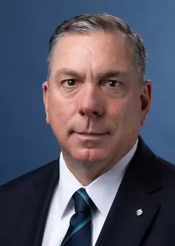 Portrait photo of Maj. Michael McCusker in a black suit with white dress shirt and a blue and teal tie.