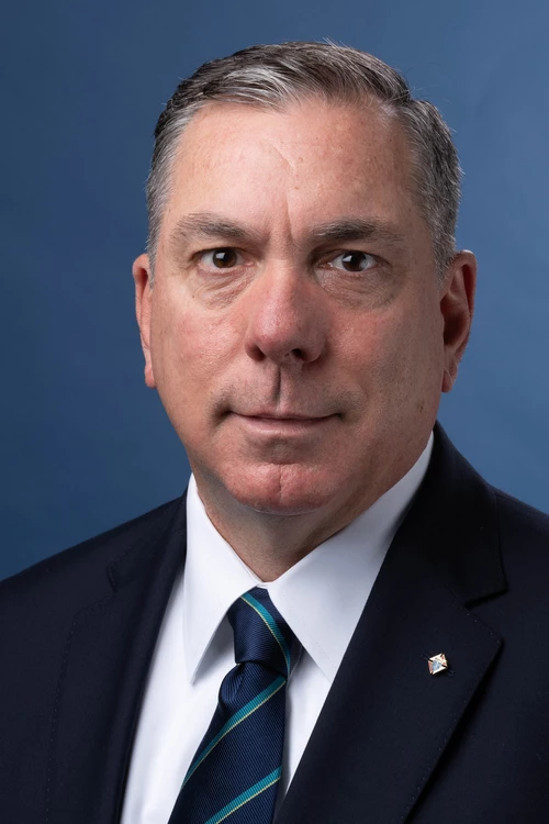 Portrait photo of Maj. Michael McCusker in a black suit with white dress shirt and a blue and teal tie.