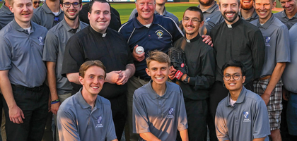 Michigan State Deputy Barry Borsenik (center, holding baseball) gathers with priests and seminarians from the Diocese of Lansing at Jackson Field for the 25th annual K of C Vocations Night baseball game. Priests, seminarians, religious sisters and numerous families enjoyed cheering on the Lansing Lugnuts, a Minor League Baseball team, and raising awareness of vocations in the Catholic Church. (Photo by Michael Back)