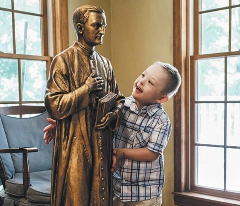 Mikey Schale looks up and smiles at a statue of Father McGivney.