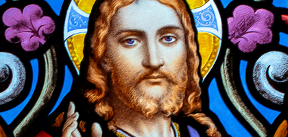 Stained glass of Jesus for the Novena to the Sacred Heart. Jesus stands with his hand up in blessing in a colorful stained glass image crop.