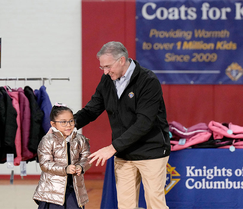 Supreme Knight Patrick Kelly helps Lexi Cordova, a first grader at Annunciation Catholic School in Denver, try on a special golden coat commemorating the 1 million coats donated