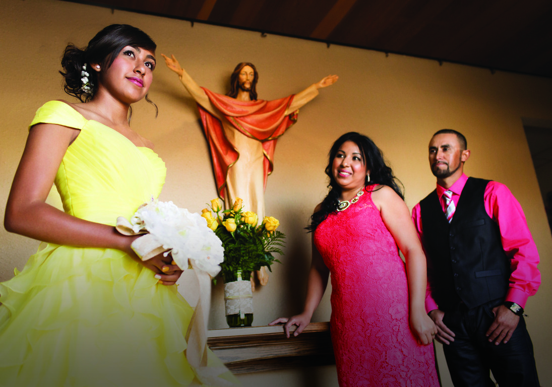 Young woman wearing a yellow dress and holding a bouquet of flowers standing next to her smiling parents.