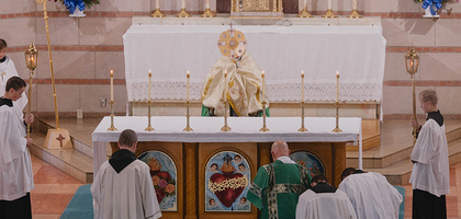 Priest and alter servers kneel facing a monstrance at an alter in church.
