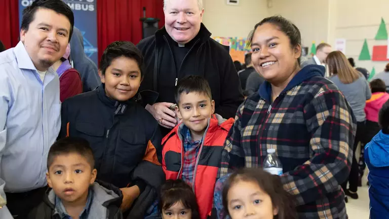 Priest with family wearing new coats at Knights of Columbus sponsored Coats for Kids event