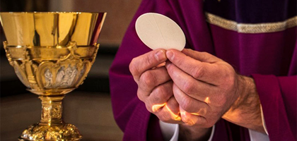 A chalice rests on the altar while the priest holds up the Host.
