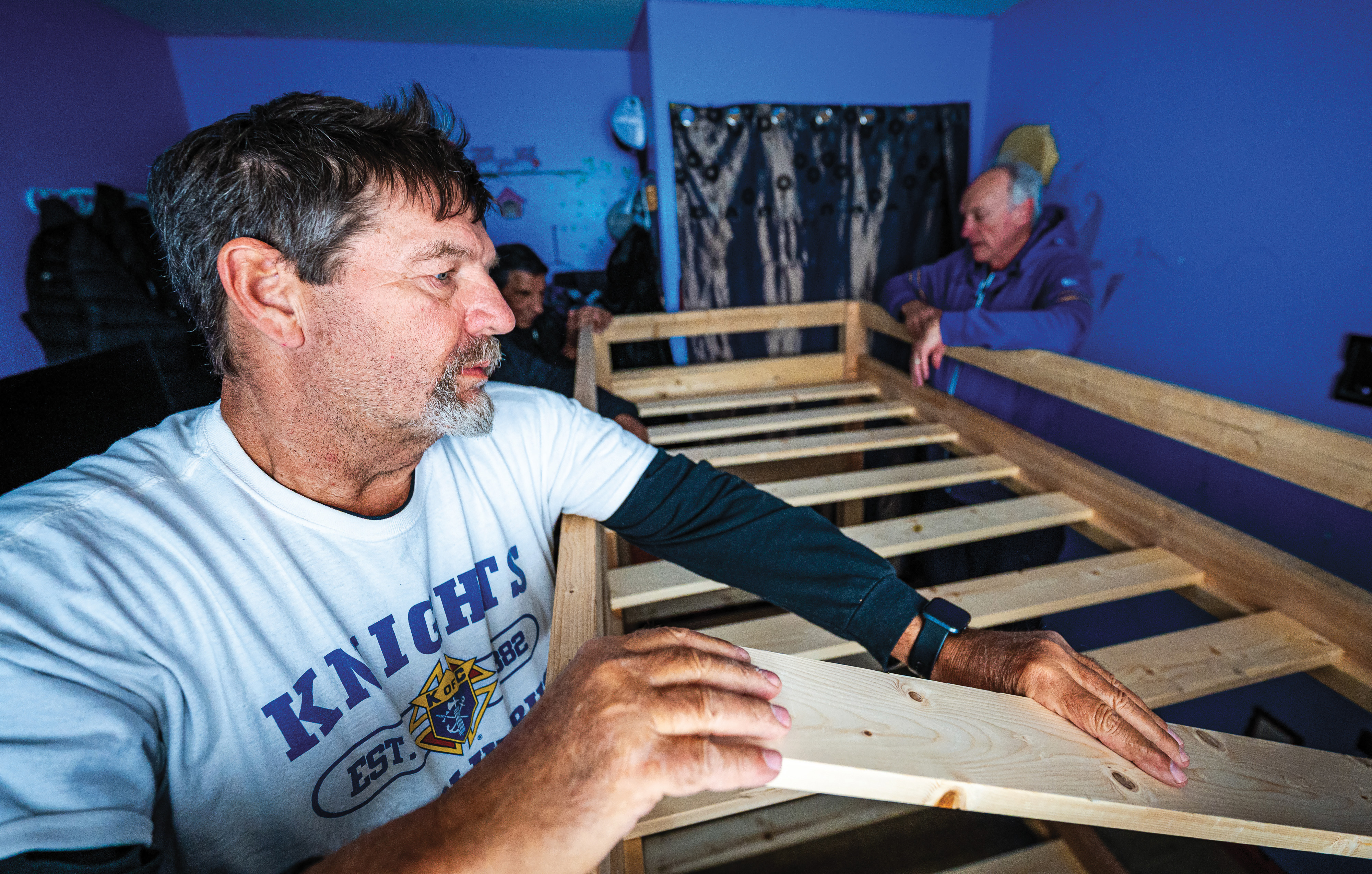 Past Grand Knight Tony Kusiak of Fathers A & J Kulawy Council 9790 places wooden slats into a new bed frame in a Pukatawagan home.