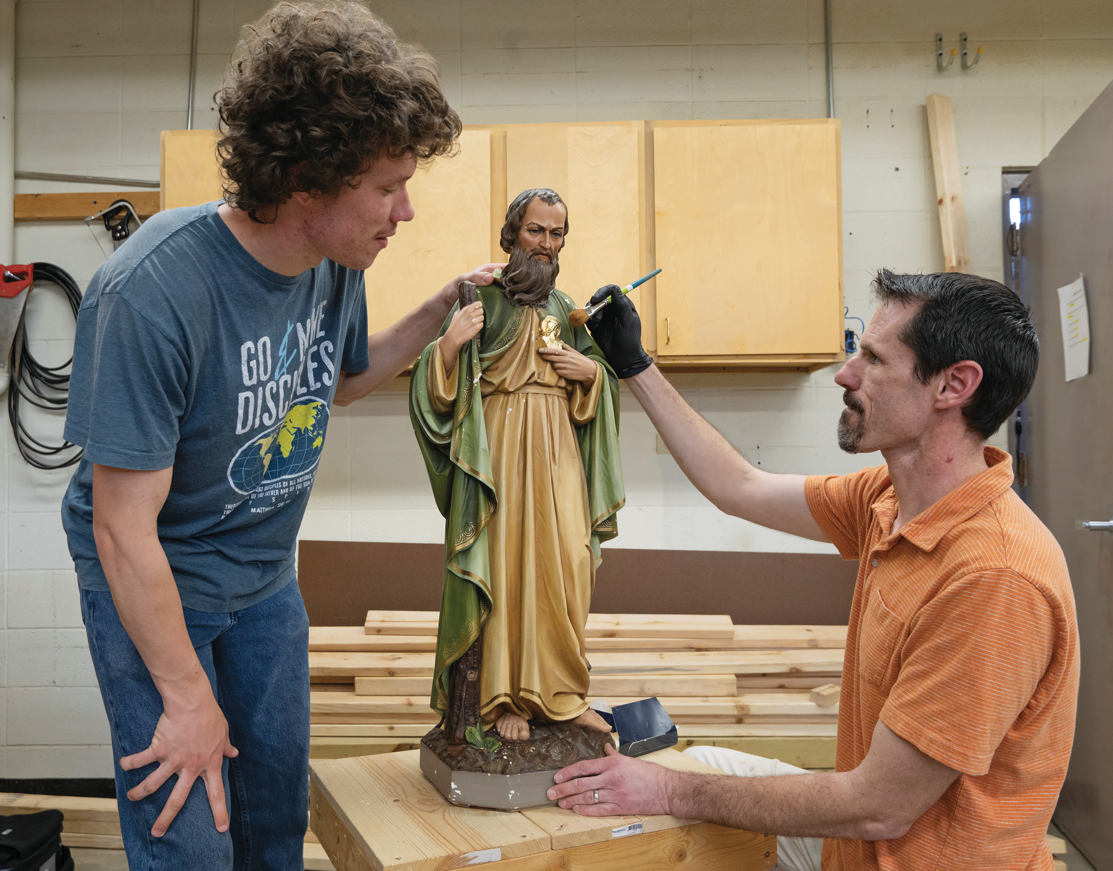 San Damiano student Joseph Lee (left), observes as instructor Joseph Williams applies gold leaf to a statue of St. Jude.