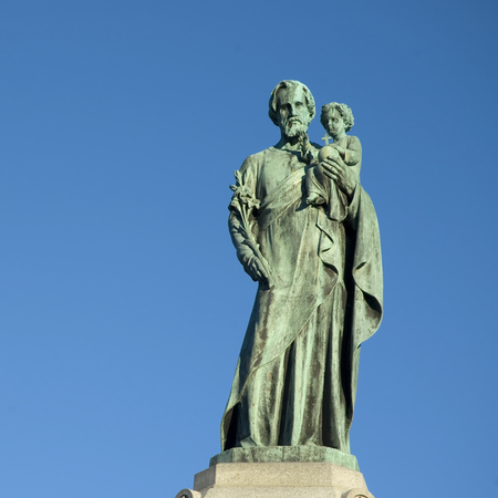 Statue of Saint Joseph holding Jesus over a blue sky.