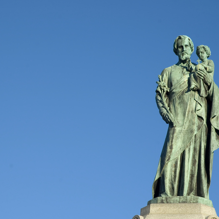 Statue of Saint Joseph holding Jesus over a blue sky.