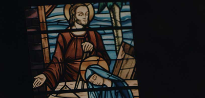 Stained glass art of Joseph accepting God's calling. Picture of a picture with wood shavings at the bottom.