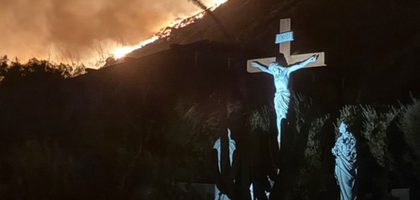A statue depicting the crucifixion sits at the bottom of  a burning mountain.