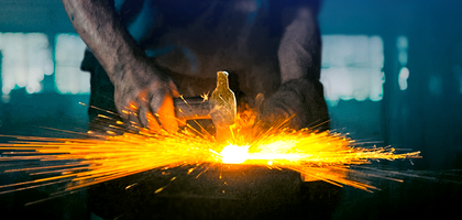 A blacksmith's hands hammer glowing metal on an anvil, sending bright orange sparks flying in a dim workshop, conveying intense focus and craftsmanship.