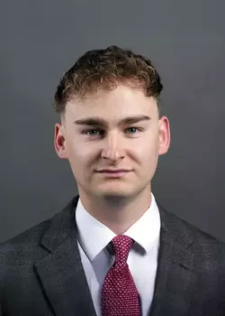 Headshot of Ty Selinske, wearing a black suit and a maroon tie.