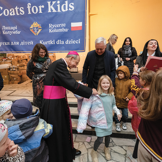 Archbishop William Lori helps a girl try on a coat during a Coats for Kids distribution for refugee children