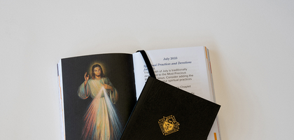 A photo of the Vivat Jesus Spiritual Planner open to an image of Jesus with another planner closed laying on top.