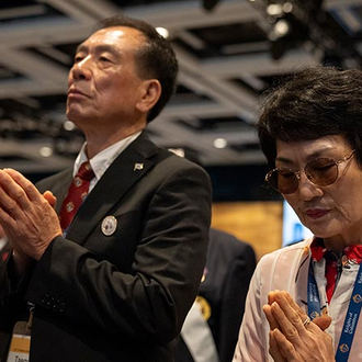 A gentleman dressed in a black suit jacket, white collared shirt, and a red tie along with a woman wearing a white and red floral blouse from the  Republic of Korea pray during the votive Mass of Sts. Joachim and Anne at the 142nd Supreme Convention in Québec City on Aug. 7.