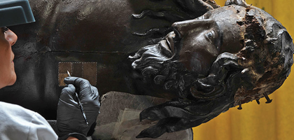 Woman holds a pencil and a grid of colors to color match the statue of Jesus Christ.