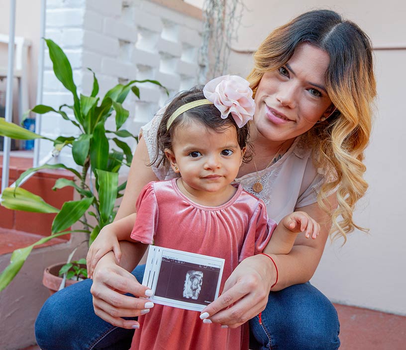A woman and child smile while the woman holds an ultrasound image.