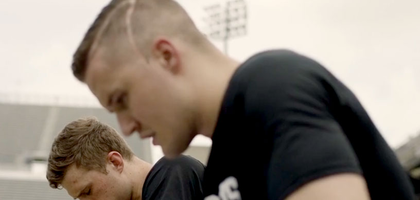 Young adult men sitting in stadium seats bow their heads in prayer.