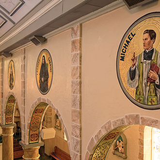 A mosaic painting of Father McGivney placed over an archway in a Catholic Church, surround by other American saints.