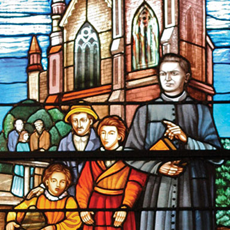 Stained glass window depicting Father McGivney shows him holding a Bible in a crowd of women and children.