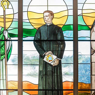 Father McGivney stands between St. Patrick and St. Thérèse of Lisieux in stained glass at Sacred Heart Catholic Church