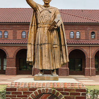 A statue of Father McGivney as he holds a Bible in one hand and raises a cross in the other outside a Roman Catholic Church