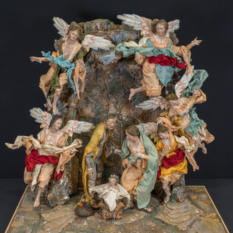 Nativity scene featuring the Holy Family and five suspended angels against a cave backdrop.