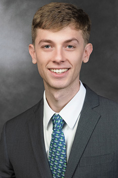 Headshot of Bradley Williams, who smiles while wearing a dark grey suit and a teal tie
