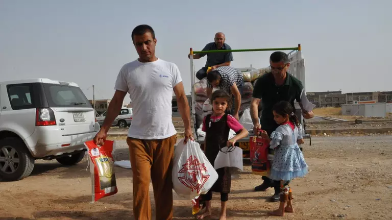 A man and two children carry supplies away from a truck.