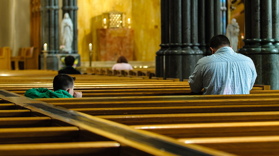 Father praying in church with son looking on.