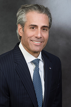 Headshot of David Calzolano, who smiles while wearing a black suit and a blue checkered tie