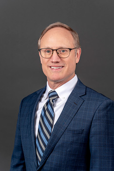 Headshot of David Hanna, who smiles while wearing a dark blue suit and a blue striped tie