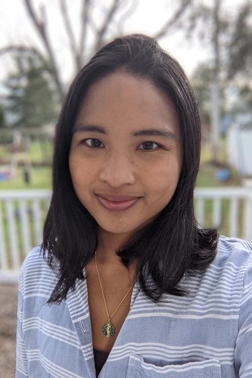 Headshot of Elizabeth Hansen wearing blue striped shirt and trees blurred in the background
