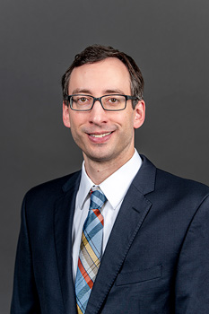 Headshot of Eric Eaton, who smiles while wearing a dark blue suit and a blue, yellow, and burnt orange plaid tie