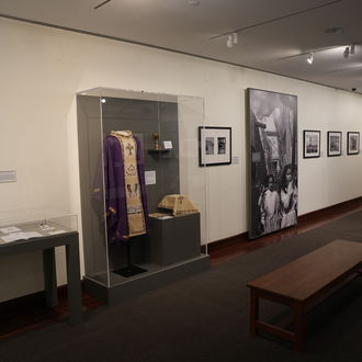 Color photo of a museum gallery with black and white photographs and items related to the 2021 visit of Pope Francis to Iraq on exhibit.