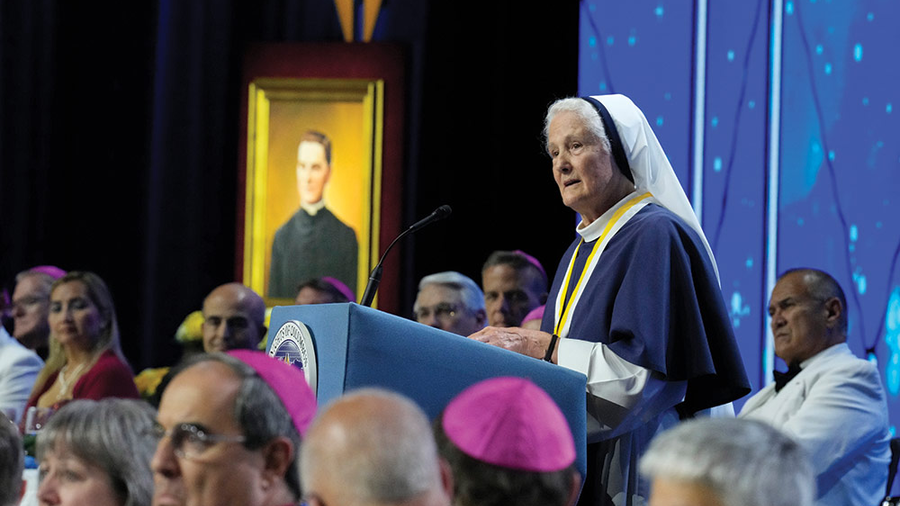Mother Agnes Mary stands at the podium looking at the Convention attendees