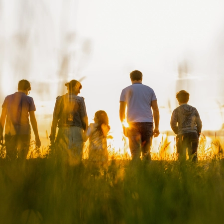 A family walking through a grass field with a sunset in the background.