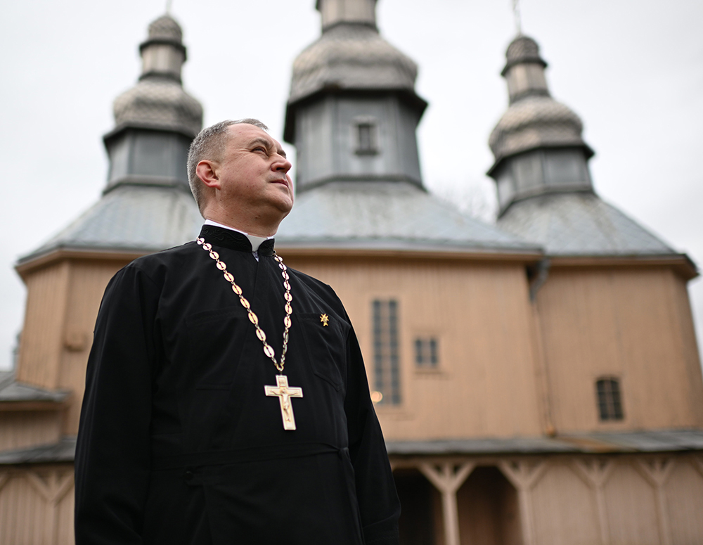 Priest stands in front of a church.
