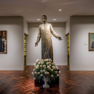Statue of Father Michael J. McGivney in the McGivney Gallery at the Blessed Michael McGivney Pilgrimage Center, with portraits of him on either side.